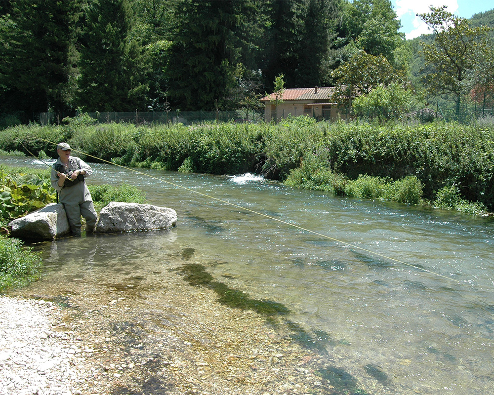 man in river fishing for trout in tuscany